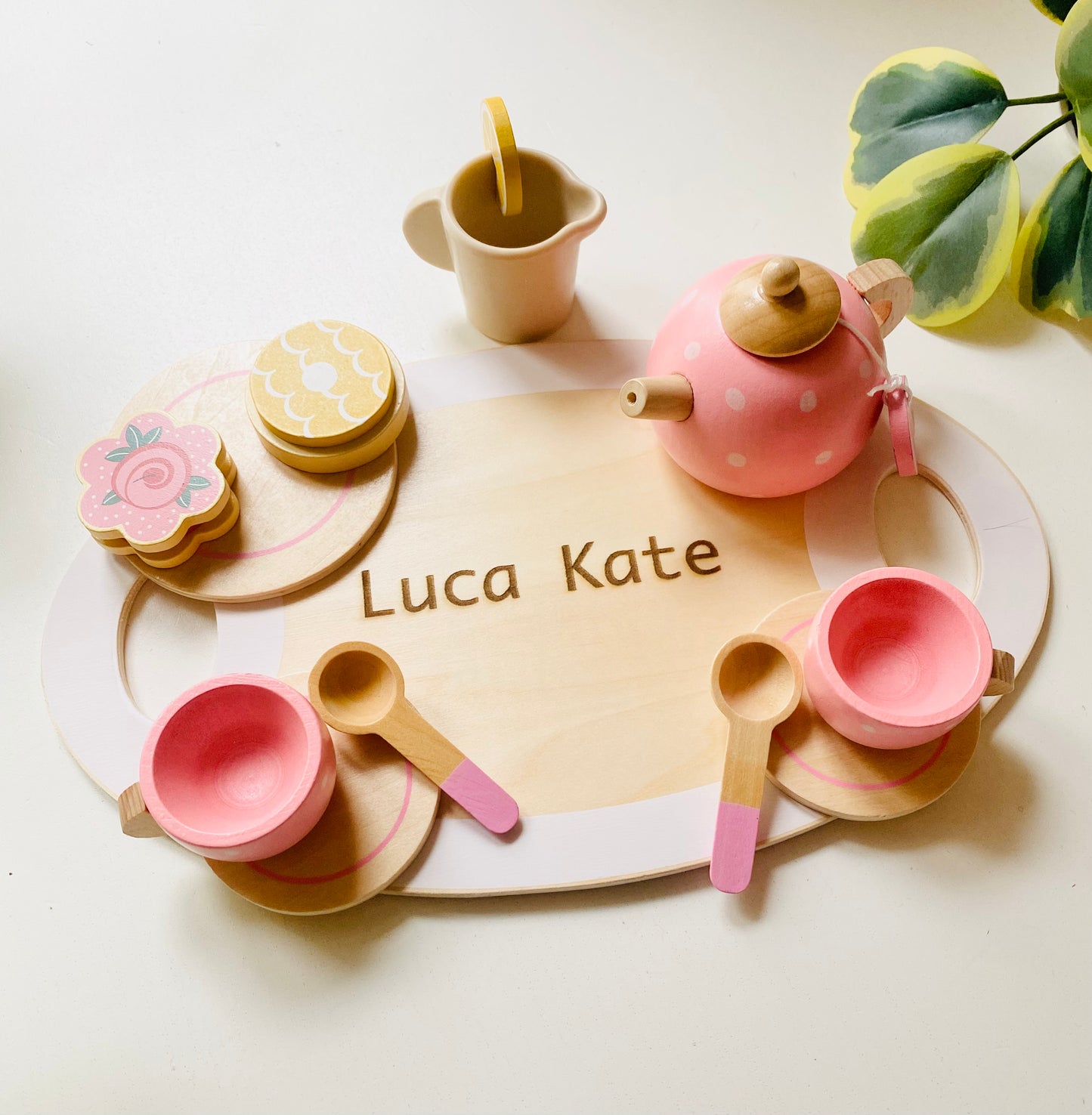 A wooden serving tray with engraving. Two pink wooden cups with saucer and spoons. A wooden pink kettle and a small tray with wooden snacks.A milk pot.