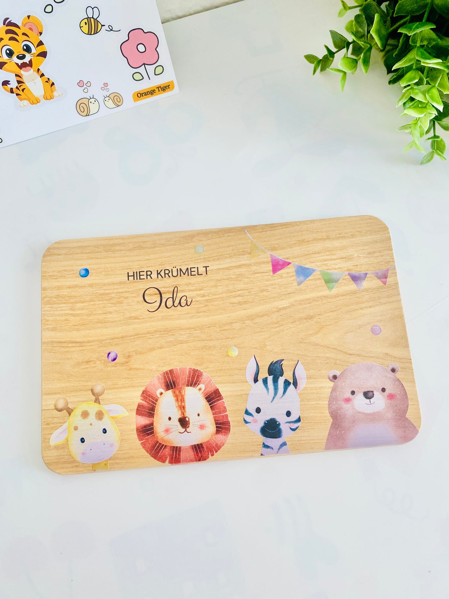 A wood snack board with "here crumble" engraving on the top. It has colorful animal motifs like giraffe, lion, zebra and bear.