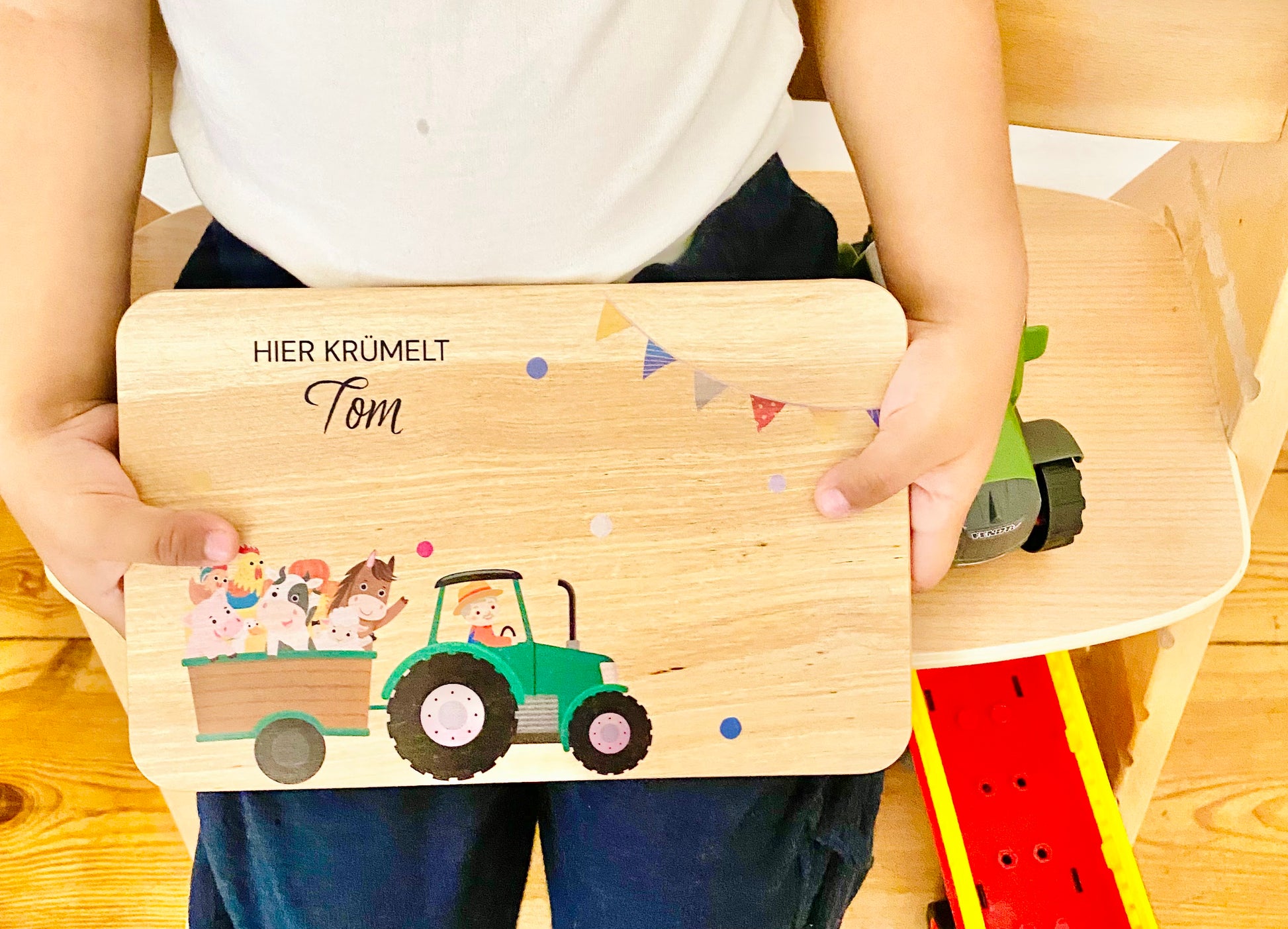 A toddler holding a beautiful breakfast board that features green farm truck with farm animals.frühstücksbretter holz