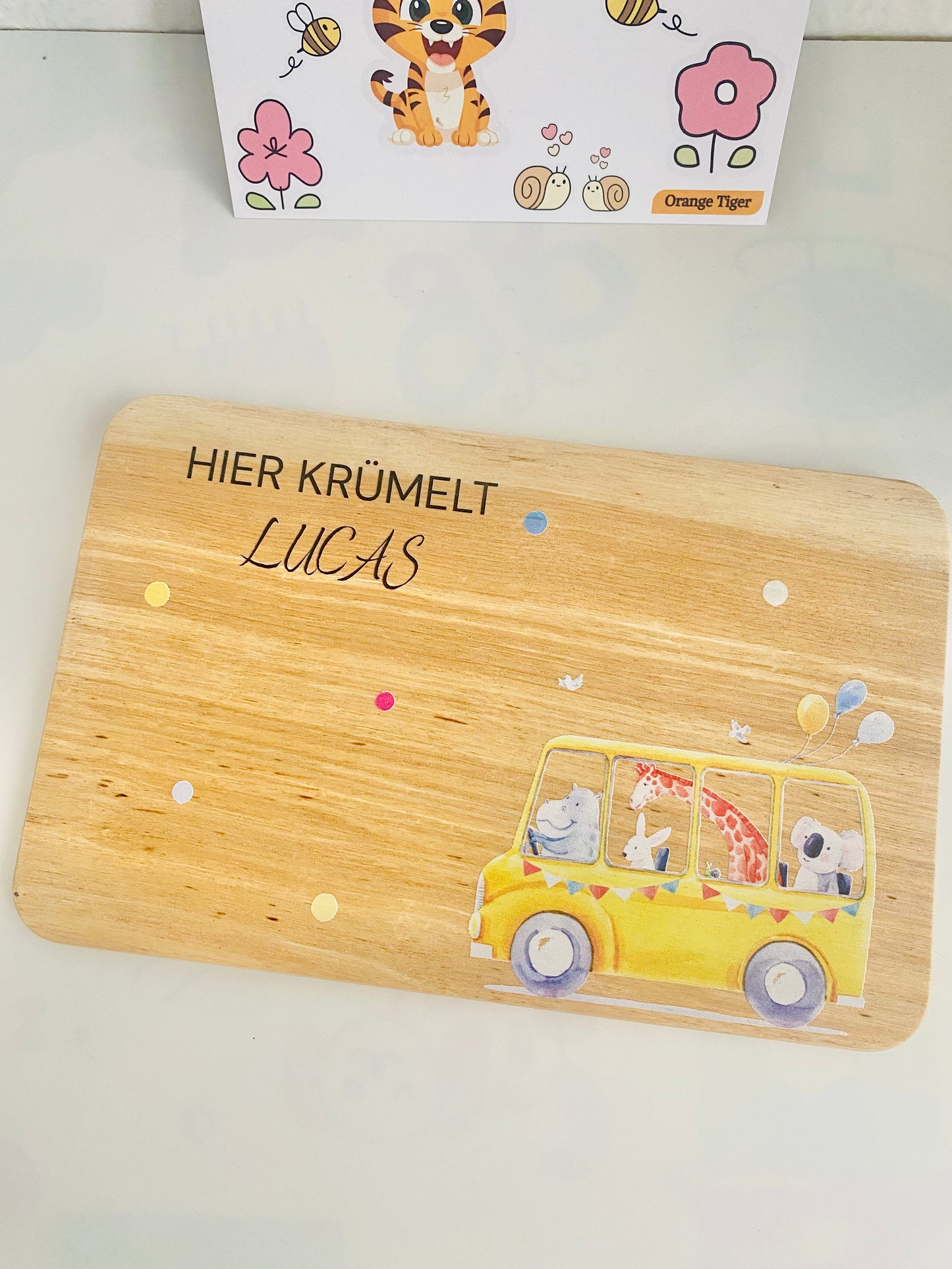 Wheels on the bus themed Brotzeit board made in beechwood. The board has colorful baloons, hippo,rabbit,giraffe ,snail and koala sitting inside the bus. "Hier Krümelt" brotzeitbrett kinder.